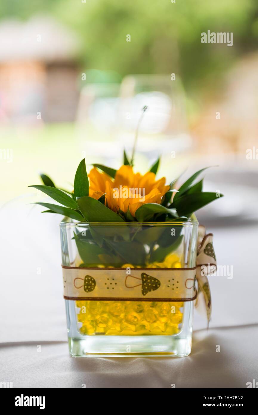 Close up of a tabletop decoration consisting in a square glass bowl containing a yellow sunflower against a bokeh background Stock Photo