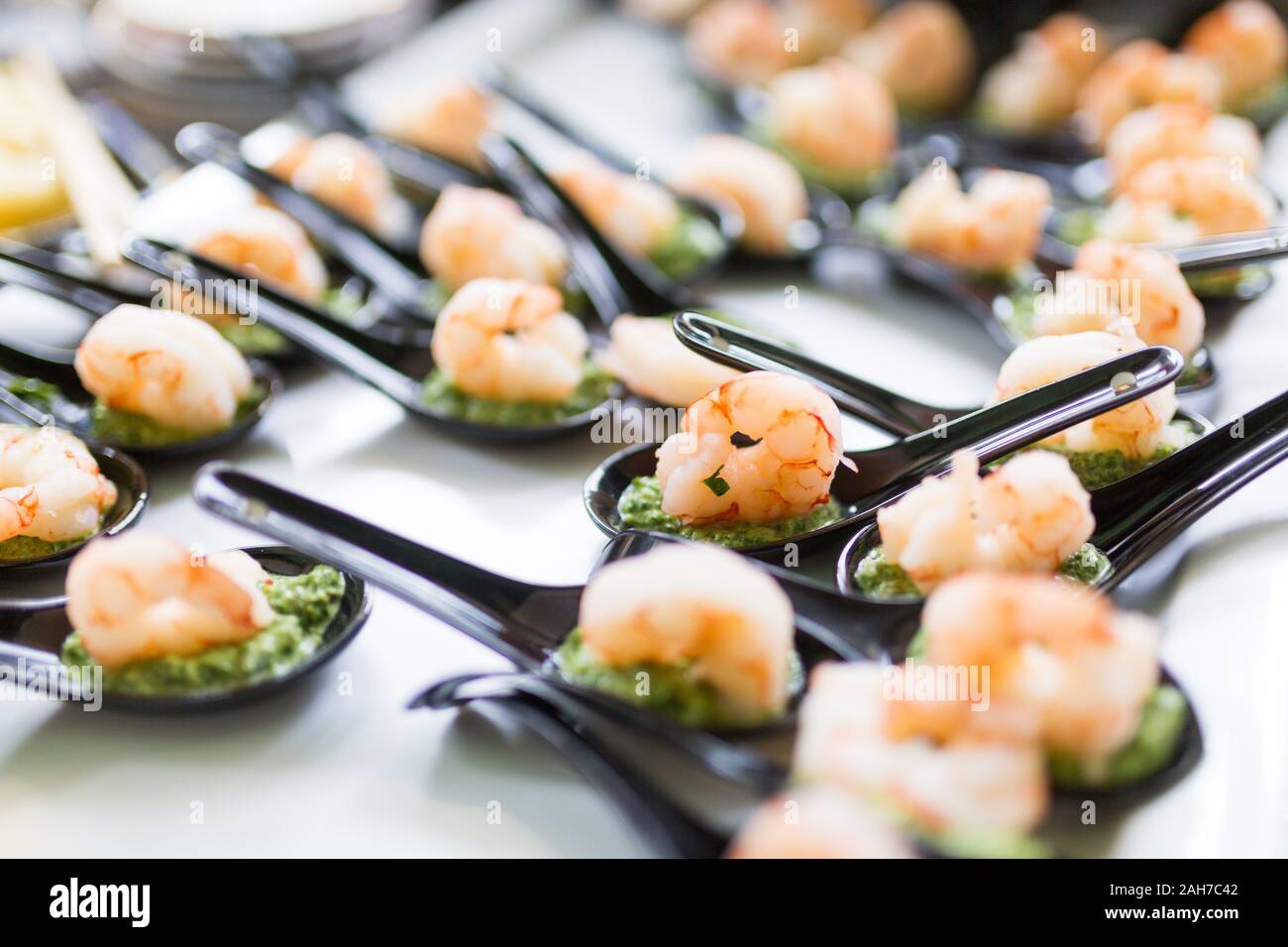 Close up of a tray holding a number of black chinese spoons each with a shrimp and some green dressing Stock Photo