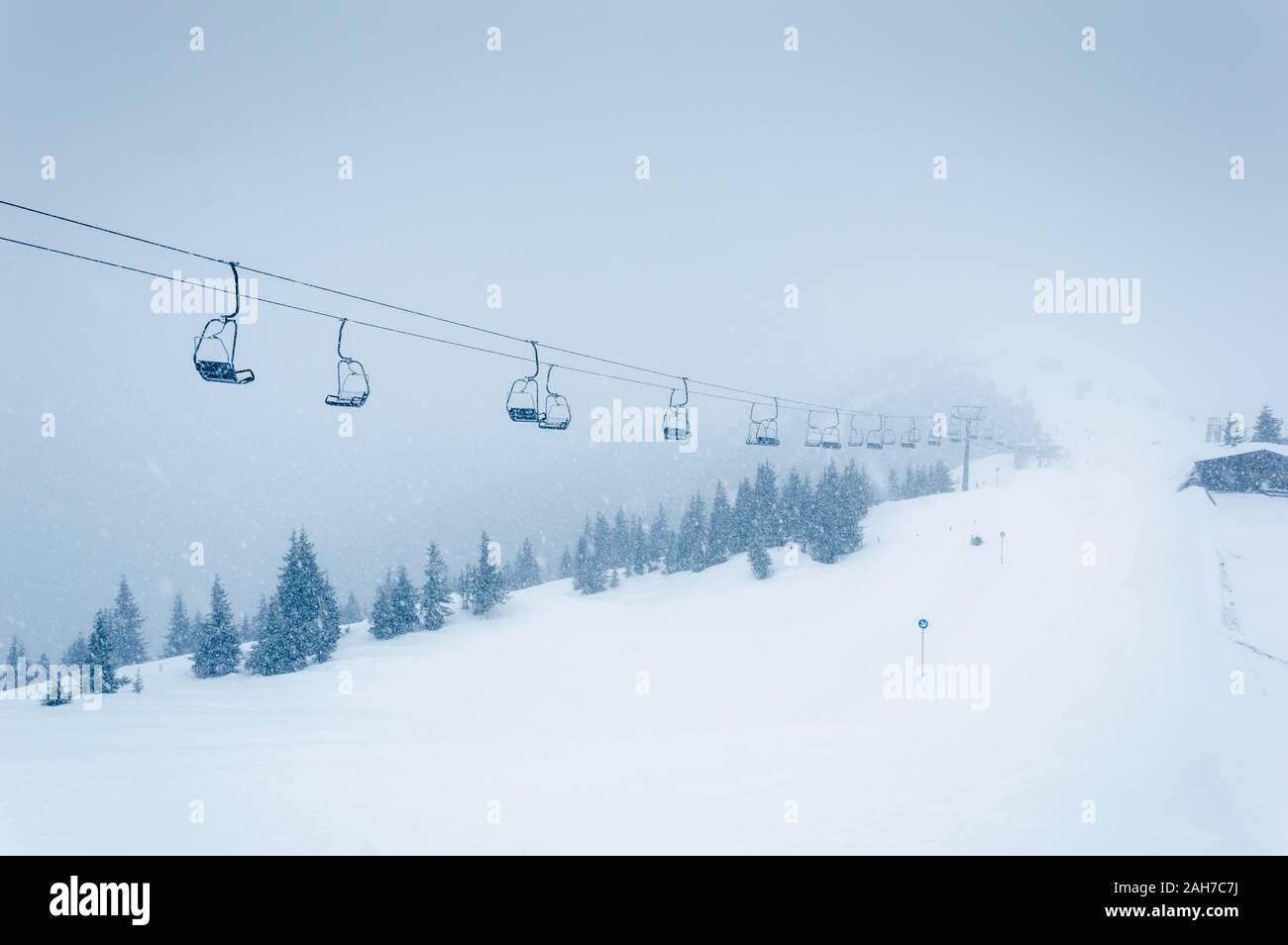 Ski lift in snowfall in mountains ski resort Zell am See Kaprun, Austria. White winter landscape with chairlifts and ski piste with snow and fir tree Stock Photo