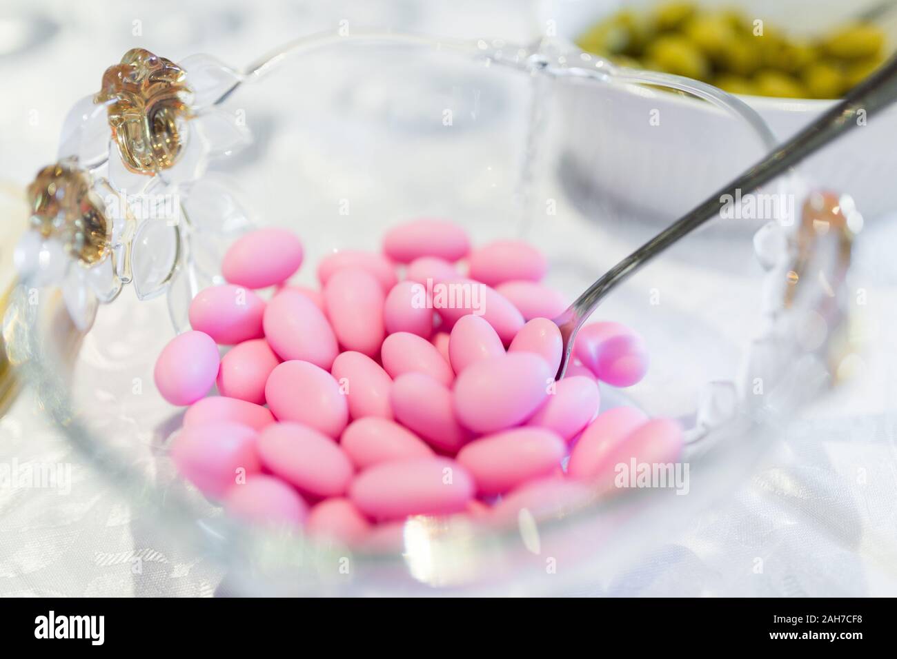 Close up of a glass cup with pink Jordan almonds and a teaspoon, against a bokeh background Stock Photo