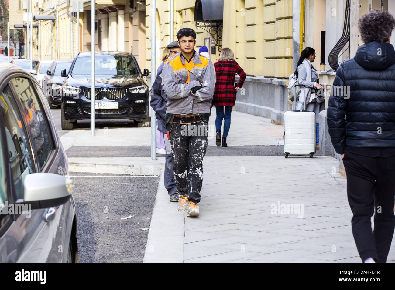 Young worker from Central Asia dressed in workwear walks on street in downtown Moscow in lunch time amid posh cars on a nice Indian summer Sept day. Stock Photo