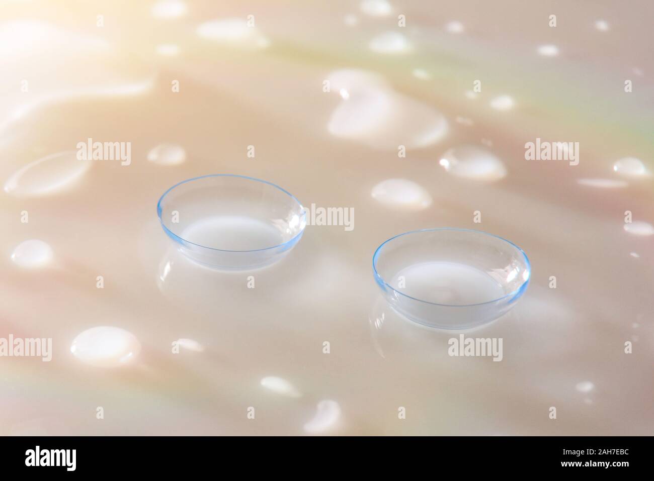 Contact lenses on white glass reflective table with water drops and color reflections. Horizontal composition. Elevated view. Stock Photo