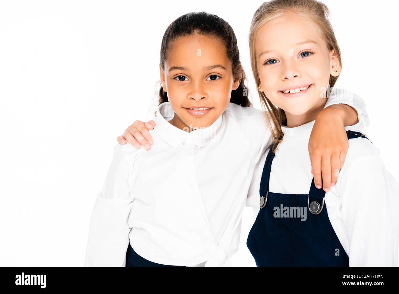 two happy multicultural schoolgirls hugging and smiling at camera isolated on white Stock Photo