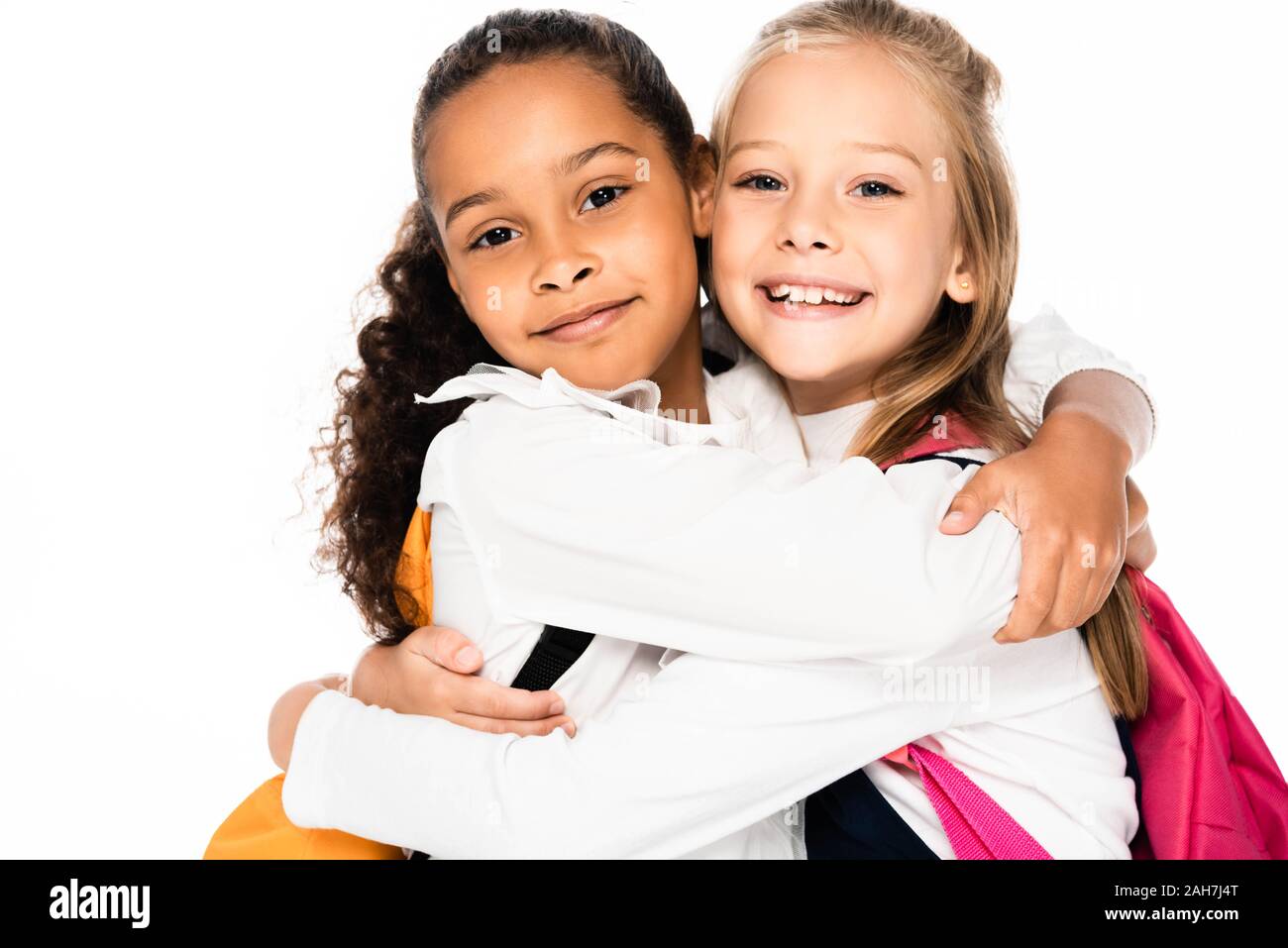 two happy multicultural schoolgirls hugging while smiling at camera isolated on white Stock Photo
