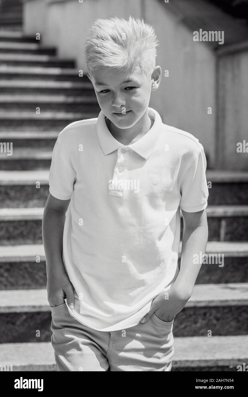 monochrome (black and white) portrait of cute handsome blonde eleven old boy (teenager) sitting on the stairs outdoor.Growing up, chilhood, separating Stock Photo