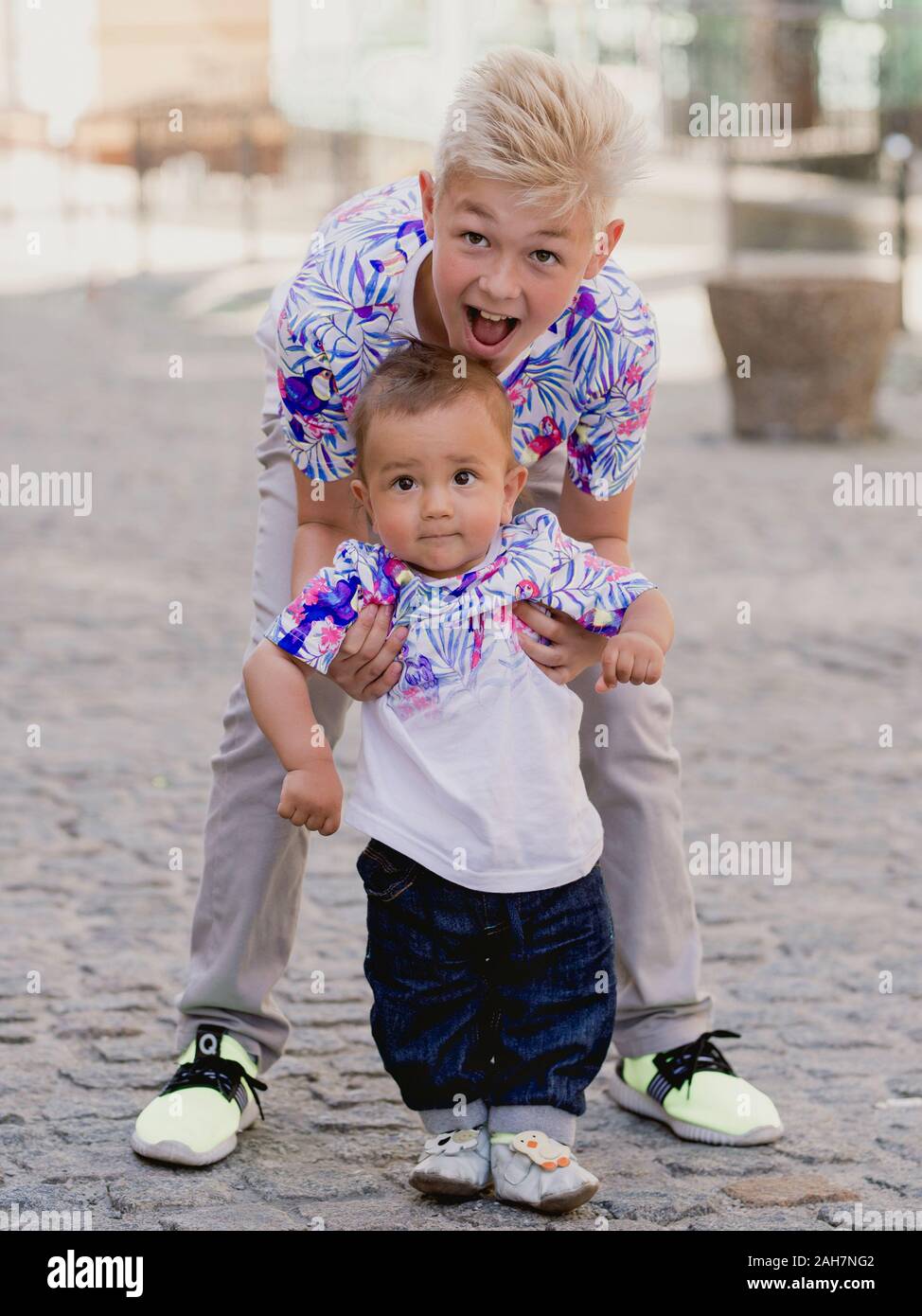 caucasian adorable cute boys siblings - one helhing another to make first step. Family, help, support concept Stock Photo