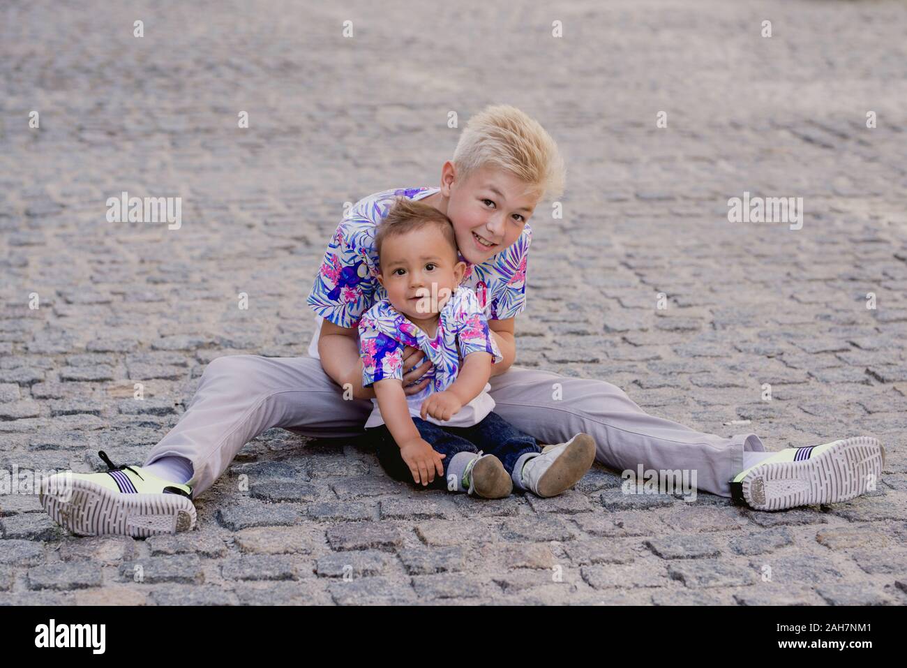 caucasian adorable cute boys siblings - one helhing another to make first step. Family, help, support concept Stock Photo