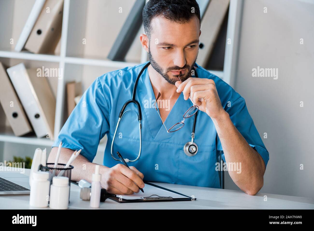 pensive doctor holding pen near clipboard in clinic Stock Photo - Alamy