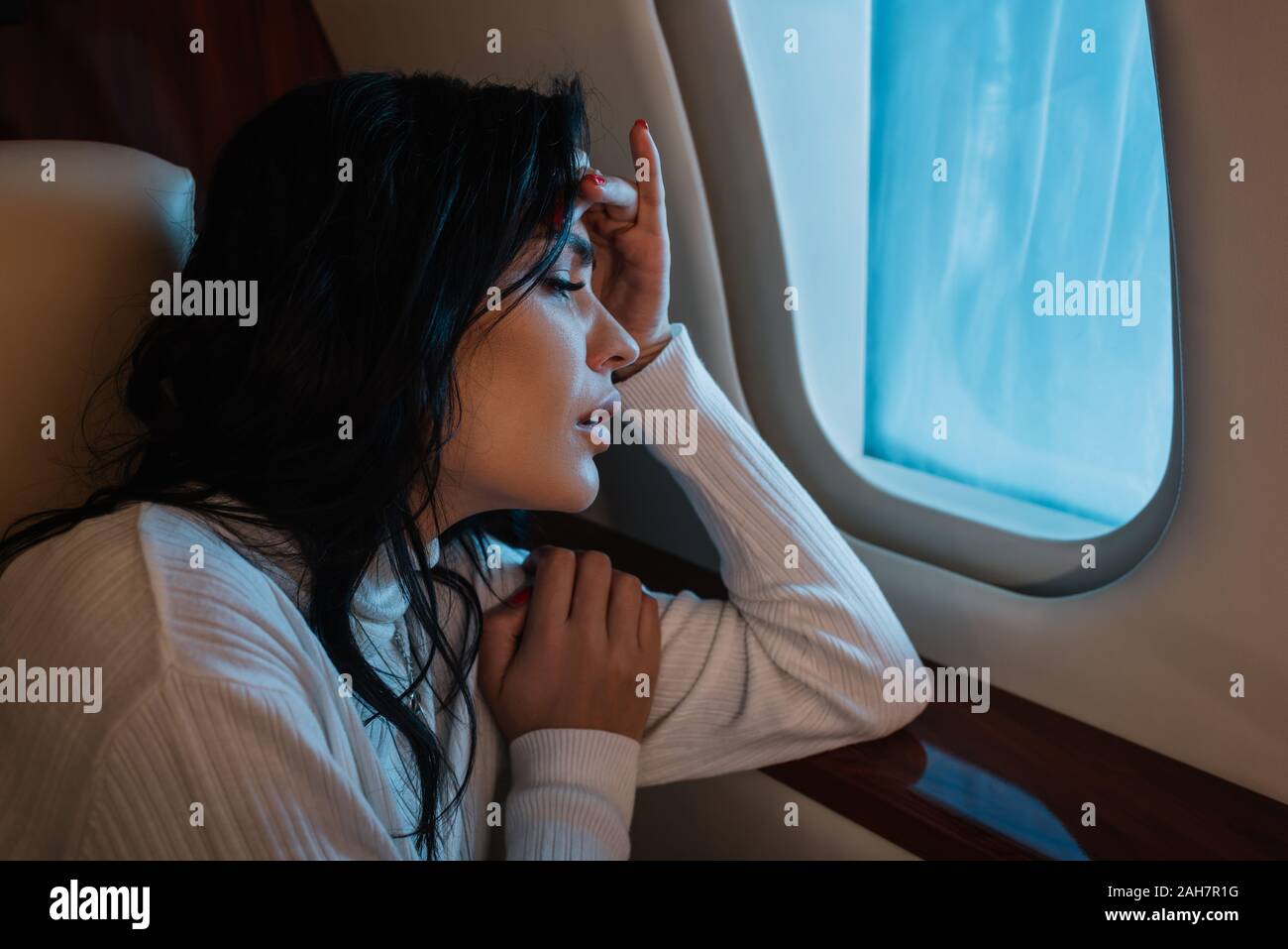 scared woman with airsickness looking at airplane window in private jet ...