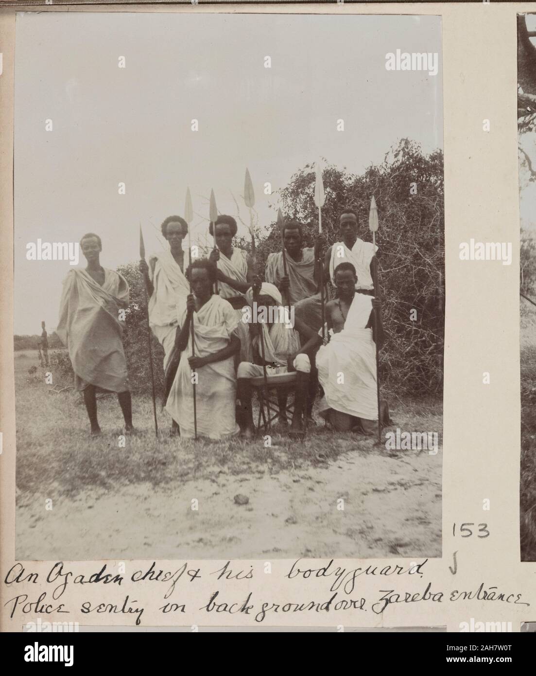 SomaliaJubaland, A group of men armed with spears surround a seated elder. A distant policeman can be seen in the background.Original manuscript caption: An Ogaden chief & his bodyguard. Police sentry in background over Zareba entrance, circa 1910. 2005/078/1/153. Stock Photo