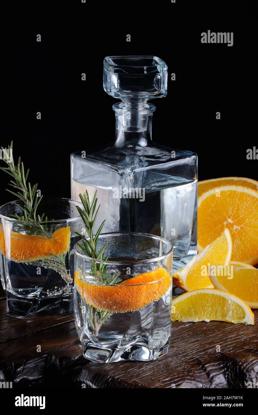Cocktail classic Dry Gin with tonic and orange zest with a sprig of rosemary on a wooden board with  slices   juicy orange Stock Photo
