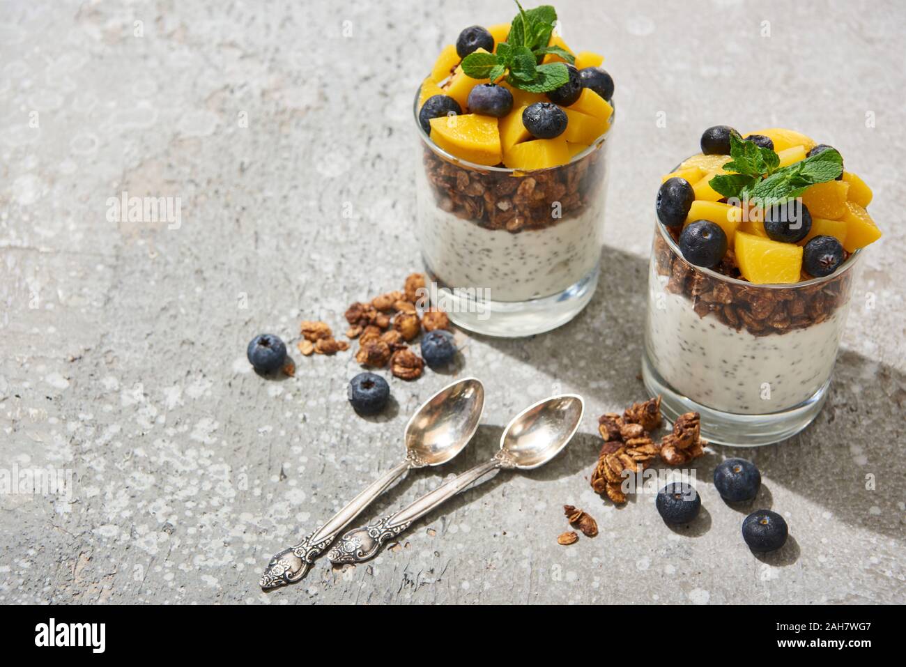 tasty granola with canned peach, blueberries and yogurt with chia seeds on grey concrete surface with spoons Stock Photo