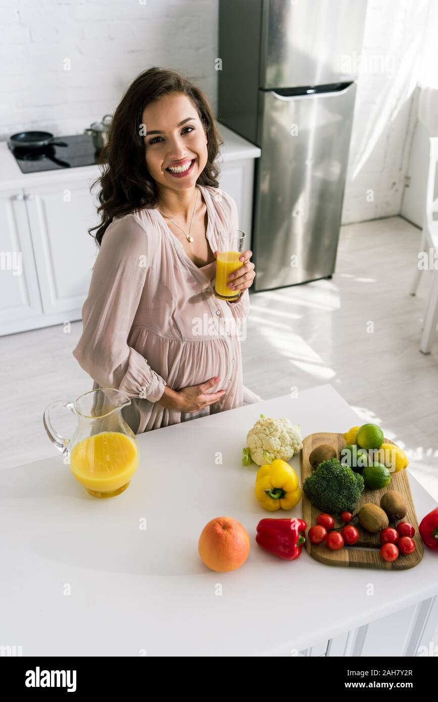 overhead view of happy pregnant woman smiling while holding glass with ...