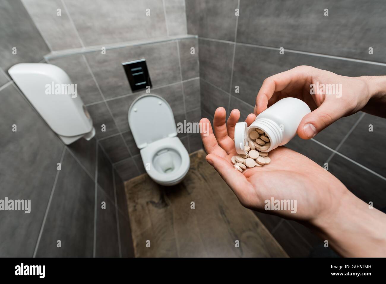 cropped view of man holding pills near ceramic clean toilet bowl in