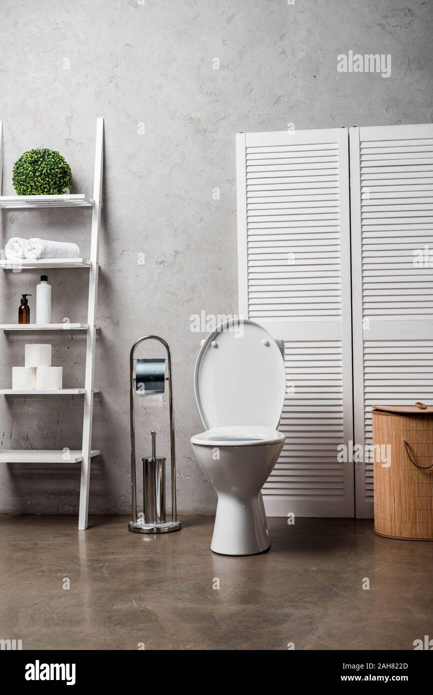 interior of modern bathroom with toilet bowl near rack with cosmetics ...