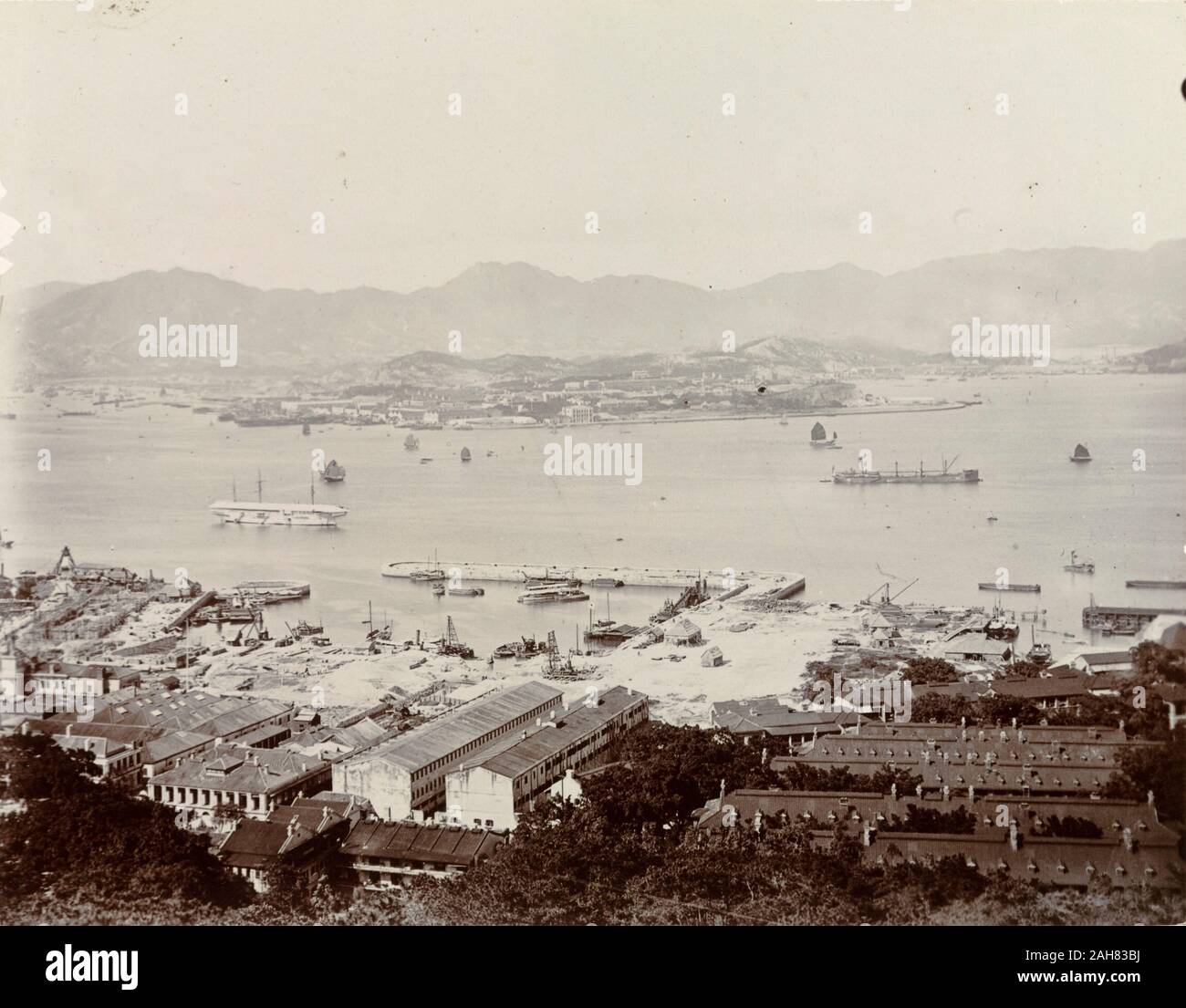 Hong KongChina, A view of Victoria Harbour, taken from Hong Kong Island and overlooking the Kowloon peninsula. A Royal Navy dockyard can be seen off Hong Kong Island, where several ships of the naval fleet are moored. Original manuscript caption: Part of Hong Kong Harbour. Man- of- War anchorage with H.M.S. 'Tamar' Depot Ship (white with roof) New naval dock in foreground. Kowloon in distance, circa 1903. 1998/028/1/1/1. Stock Photo
