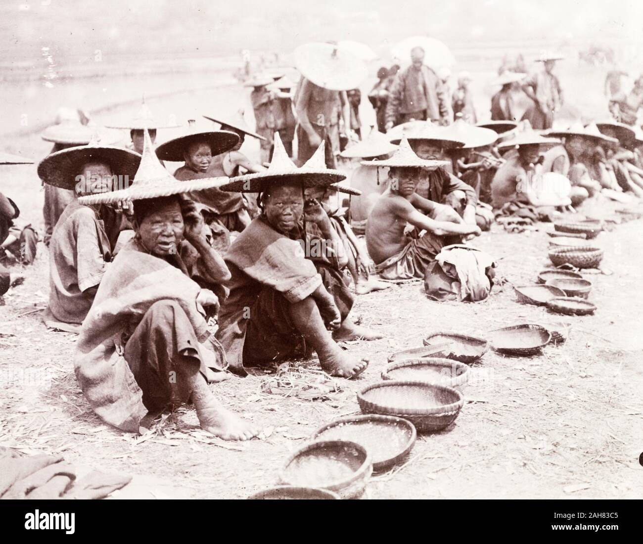 China, A number of mendicants, some of whom are suffering from leprosy, beg at the roadside with their woven bowls. Both men and women wear wide-brimmed conical hats. Original manuscript caption: Beggars and Lepers. Shikwan, circa 1905. 1998/028/1/1/27. Stock Photo