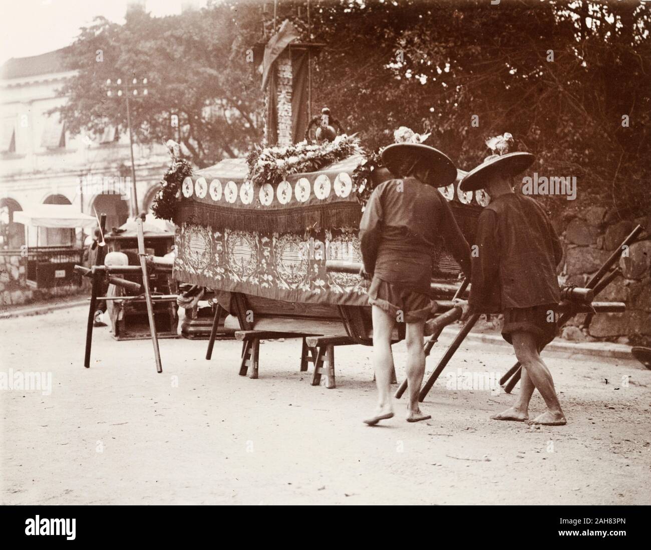 China, Two pallbearers prepare to carry a coffin on a wooden bier during a Chinese funeral ceremony. The coffin is draped in fine cloth and decorated with wreaths of flowers, indicating that the deceased had been wealthy.Original manuscript caption: Chinese funeral - (wealthy), circa 1905. 1998/028/1/1/52. Stock Photo