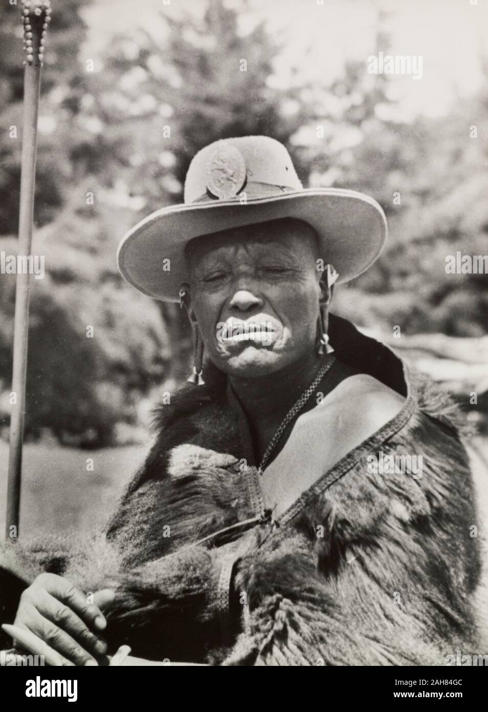 Kenya, Portrait of Chief Murigo wearing traditional Kikuyu jewellery and holding a staff. He wears a Western-style, wide-brimmed hat with a badge depicting a lion, and an animal skin wrapped around his shoulders. Original manuscript caption: Chief Murigo. Near Kakamega, 1936(Kikuyu chapter) (Chap 13)98. p37, 1937. 1995/076/1/2/5/3. Stock Photo