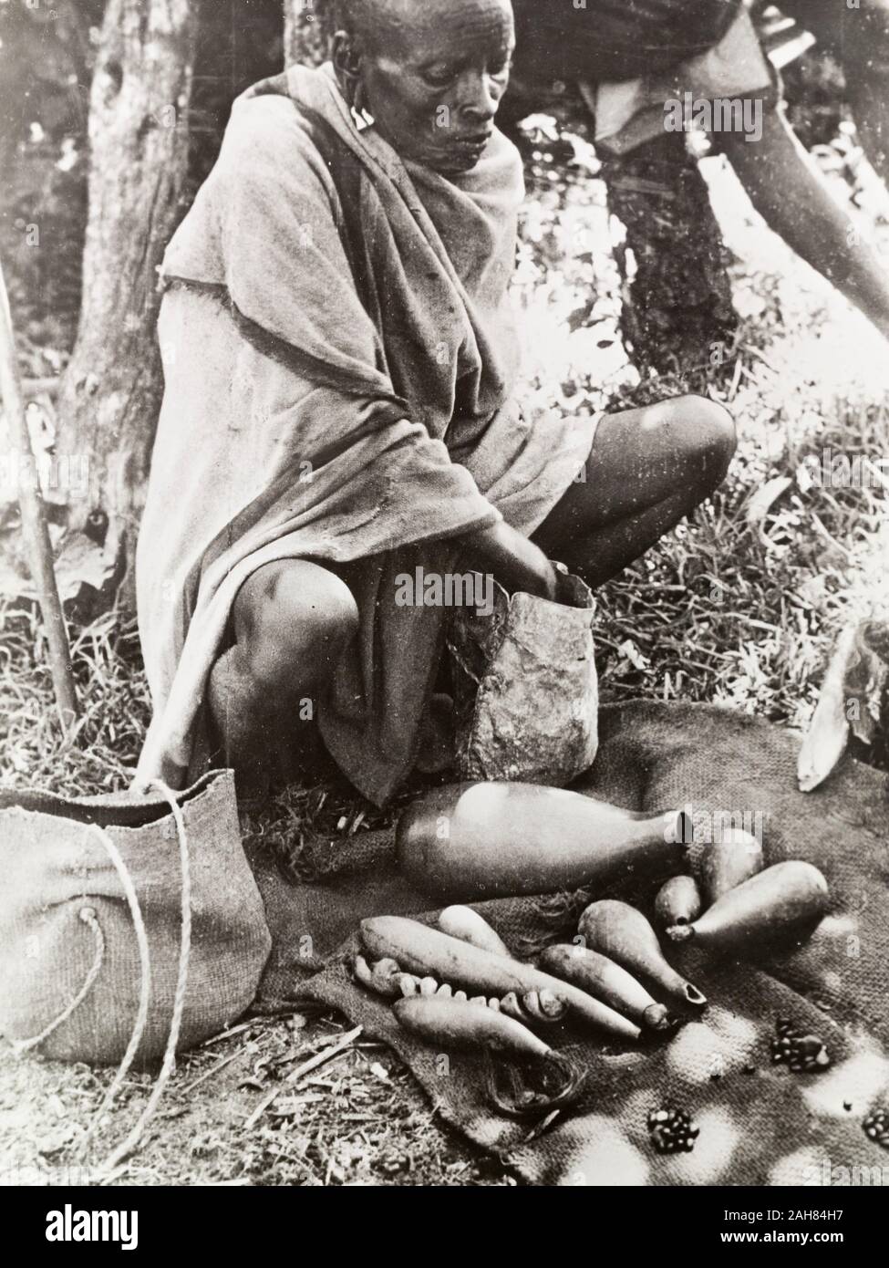 Kenya, A tribal healer prepares to tell the fortune of a client, using beans contained in a number of small stoppered gourds. Original manuscript captions: Reading the beansA witchdoctor with his beans, or stones, in small stoppered gourds, preparing to tell the fortune of a client. South Nyeri, 1936, 1937. 1995/076/1/2/5/24. Stock Photo
