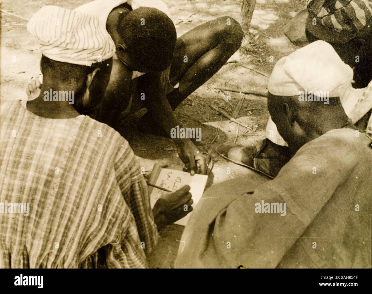 Gold CoastGhana, A student teacher helps men to read from a book during a literacy class; part of a mass literacy campaign launched by the British government in 1951 to improve literacy skills amongst African adults, both in their own languages and in English. Original manuscript caption: Mass literacy class. NTs [Northern Territories], 1951-52. 1995/076/5/2/2/36. Stock Photo