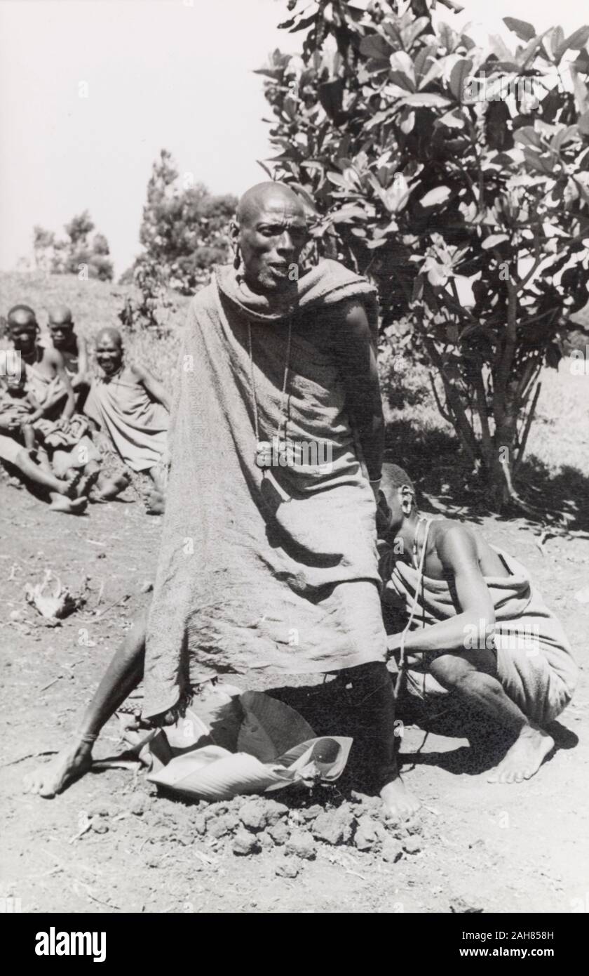 Kenya, A Kikuyu man takes part in a purification ceremony with a tribal healer.Original manuscript caption: Casting out a 'thahu', part of the Kikuyu purification ceremony. The witchdoctor stands in front of the sacrificial goat, the supplicant behind him.Near Karatina, South Nyeri, 1936, 1937. 1995/076/1/2/5/30. Stock Photo