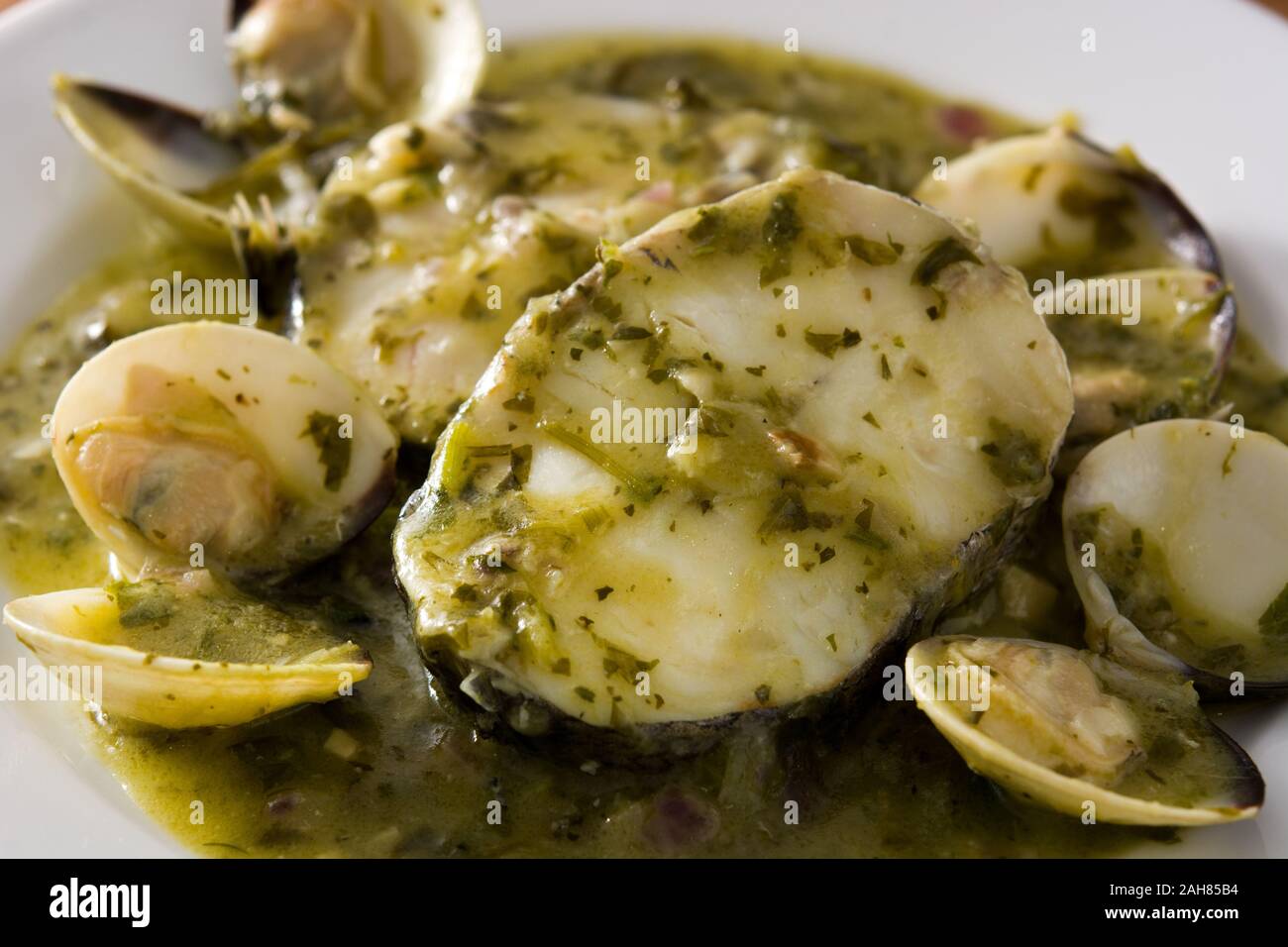 Hake fish and clams with green sauce on wooden table. Typical spanish