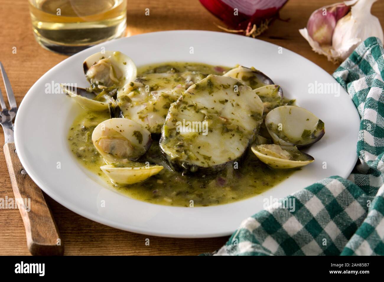 Hake fish and clams with green sauce on wooden table. Typical spanish