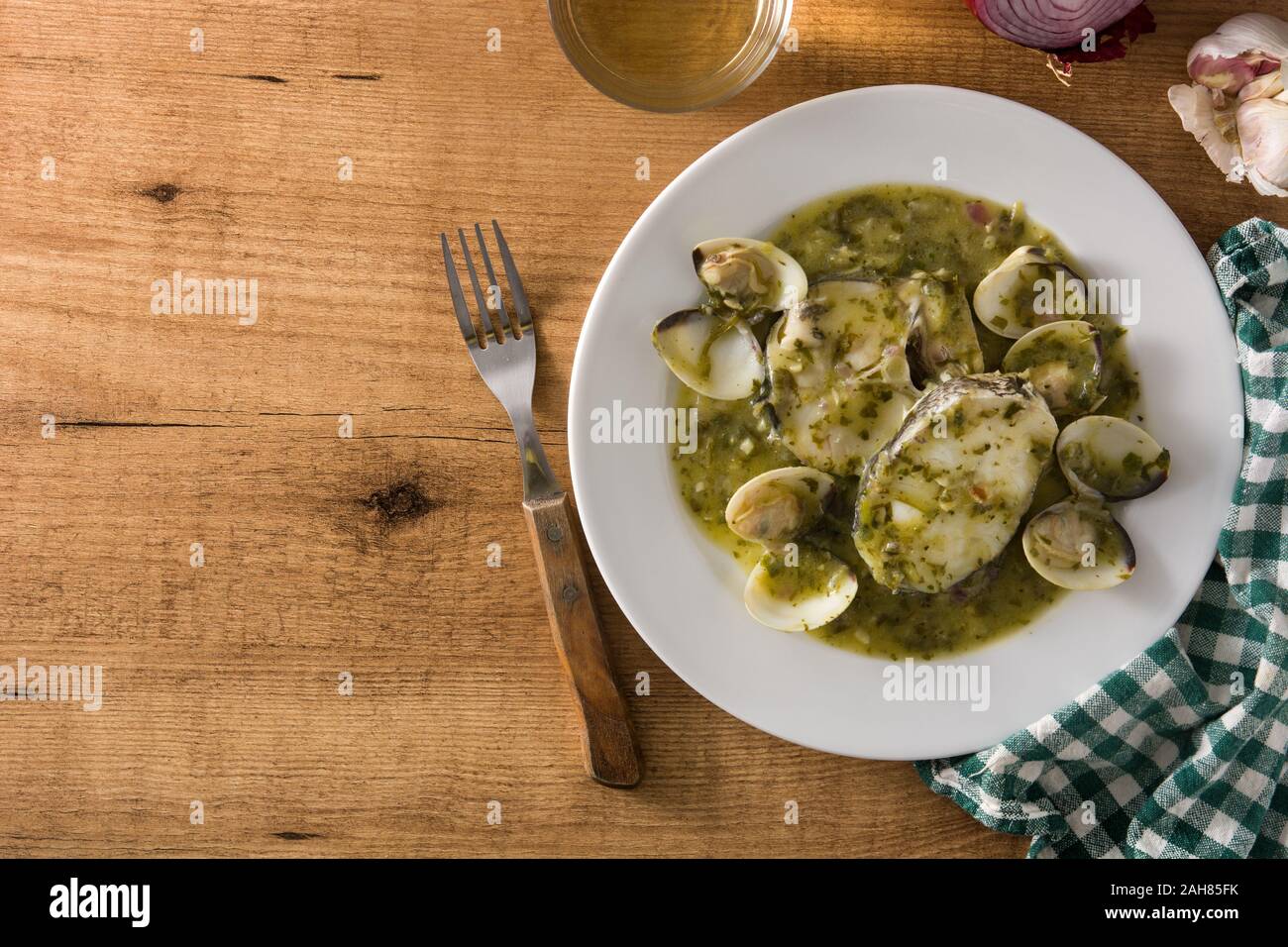 Hake fish and clams with green sauce on wooden table. Typical spanish