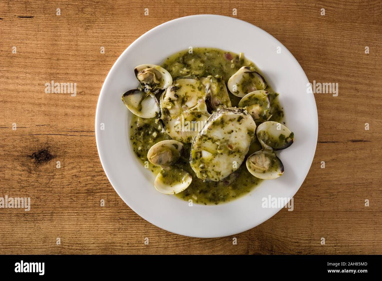 Hake fish and clams with green sauce on wooden table. Typical spanish