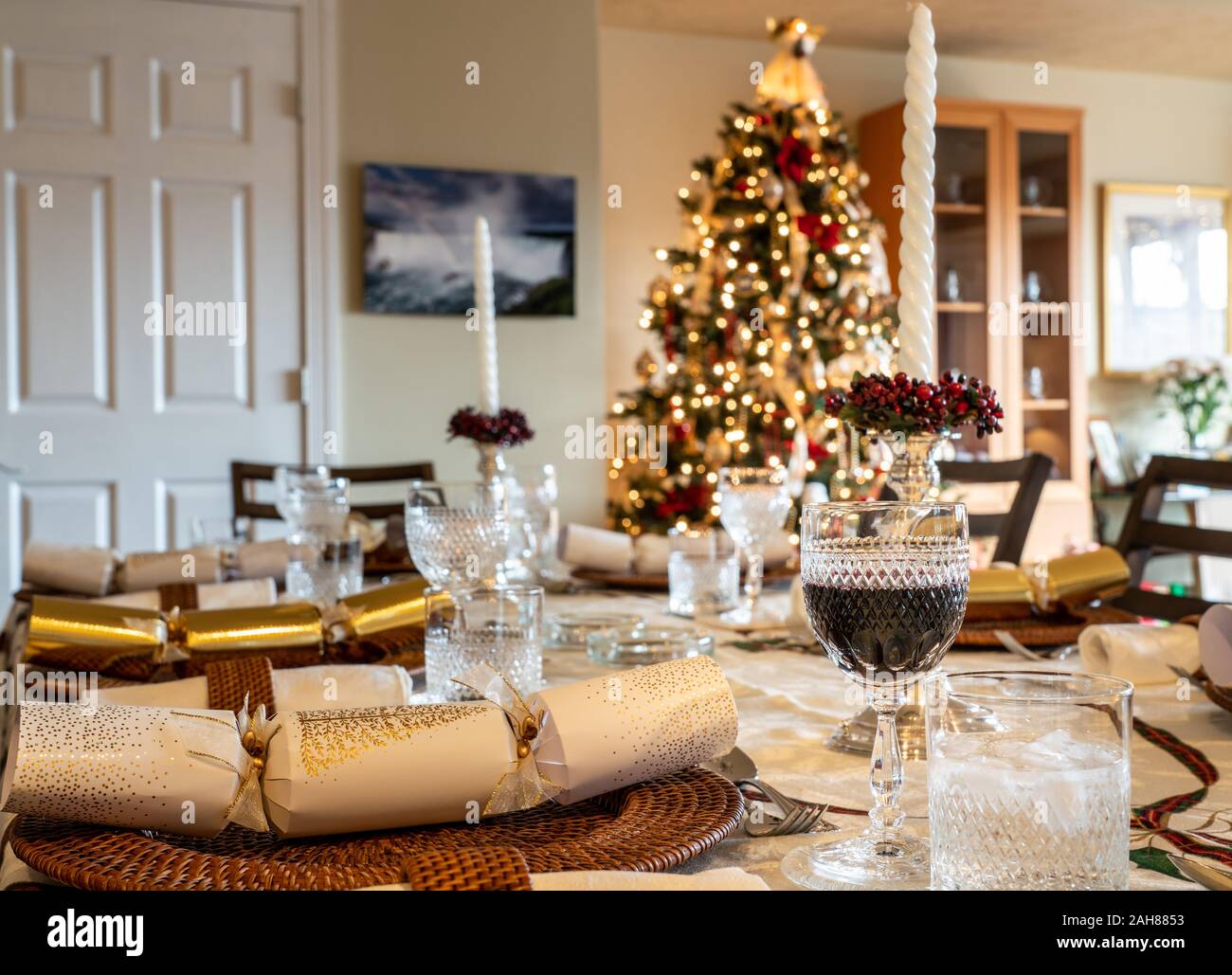 Traditional british christmas lunch table setting with crackers and glasses with xmas tree in the background Stock Photo