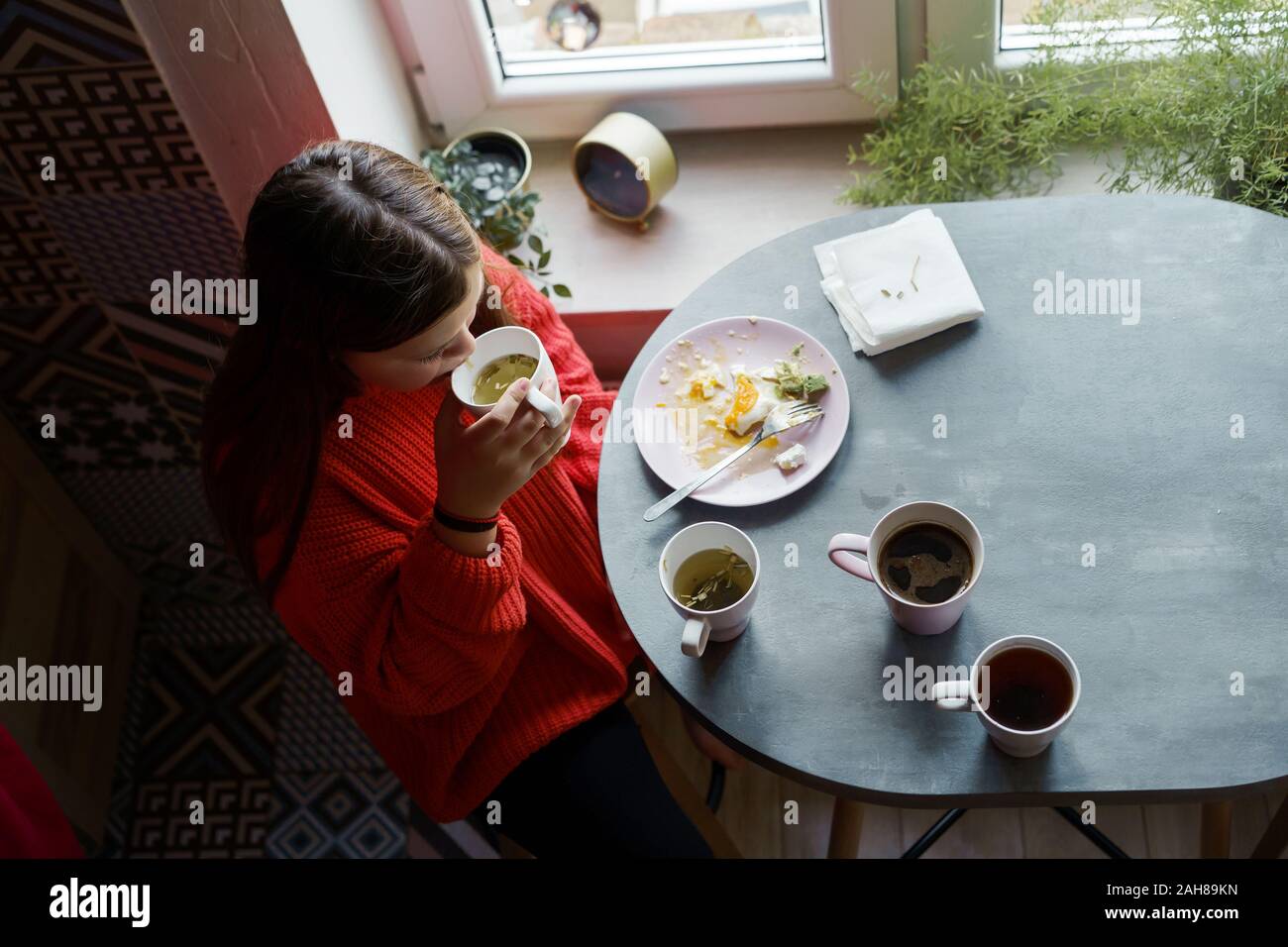 Blonde girl with long hair in a red sweater sitting at the dining table Stock Photo