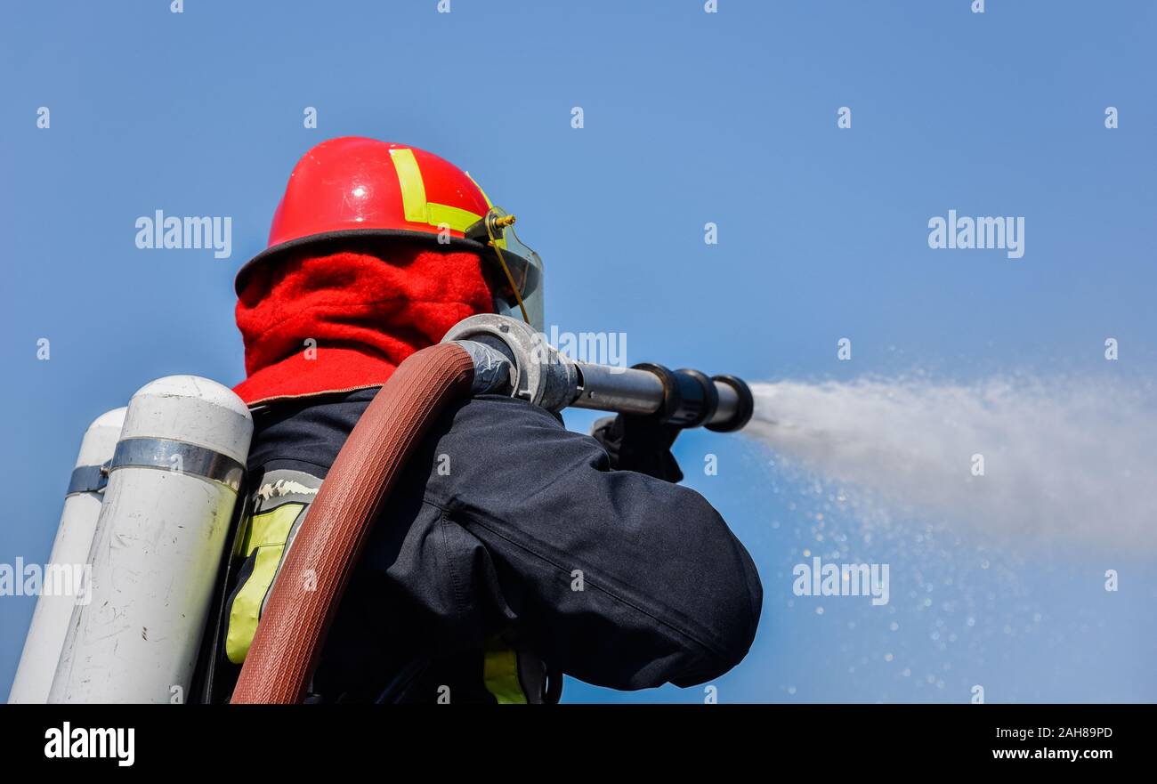 Fireman in uniform and oxygen mask spraying water Stock Photo - Alamy