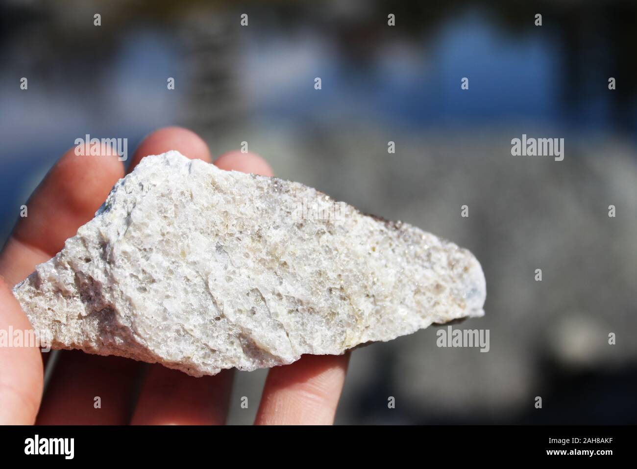 Close up hand holding rock on a background of blue water with landscape ...