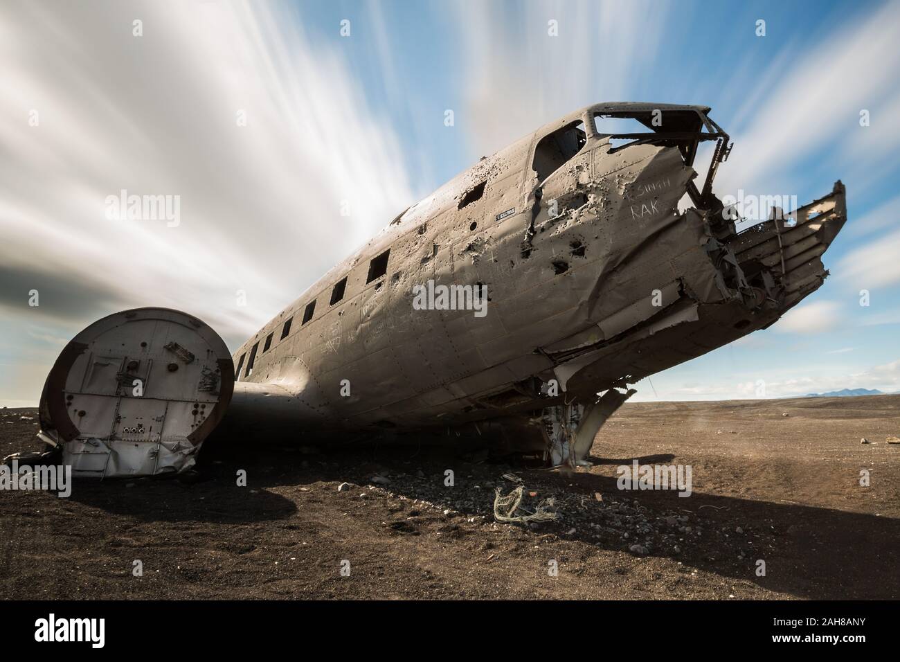 Low angle view of an abandoned DC-3 plane lying in the icelandic desert, against a blue summer sky with trailing clouds Stock Photo
