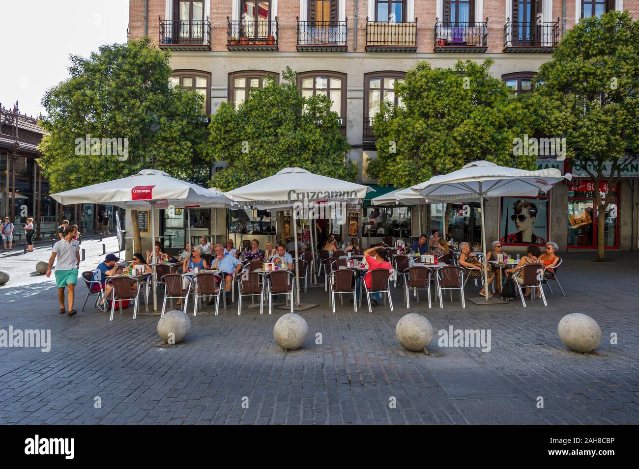 People sitting on chairs under big umbrellas eating and drinking on the pavement outside a restaurant in Madrid, Spain Stock Photo