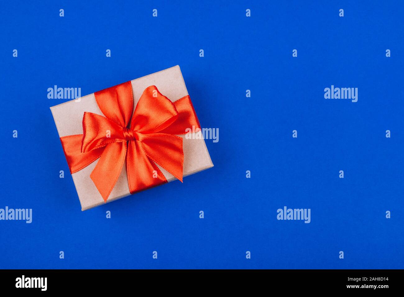 Cardboard gift box with red bow on blue background. Stock Photo
