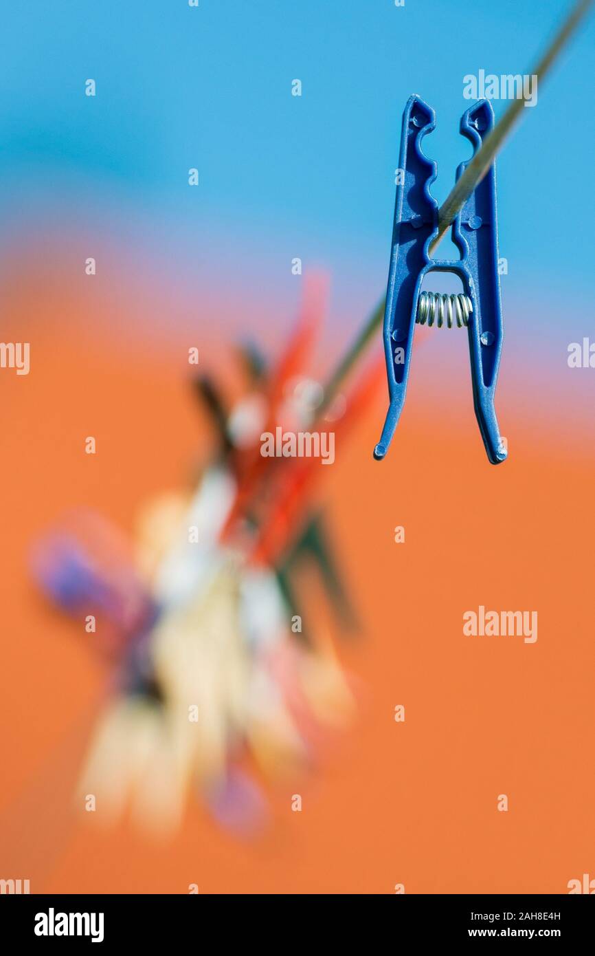 Close up of a laundy peg singled out from the others hanging from the same line, against a blue and orange bokeh background Stock Photo