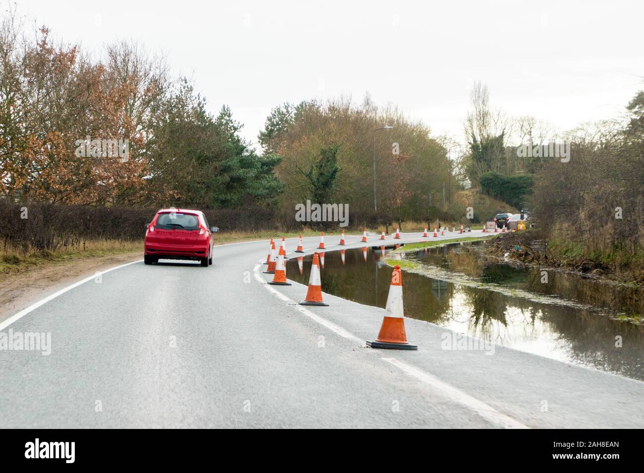 A main road through part of the United Kingdom is coned off to protect drivers from driving through a flooded lane. Stock Photo