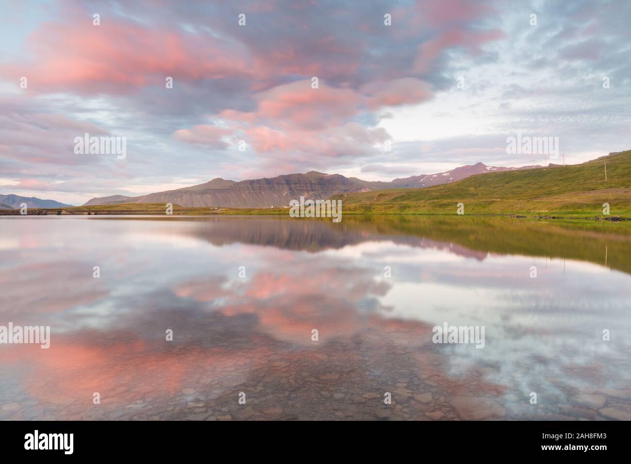 Wide angle view of a colorful symmetrical Icelandic sunset with pink clouds reflecting on the waters of a pond Stock Photo