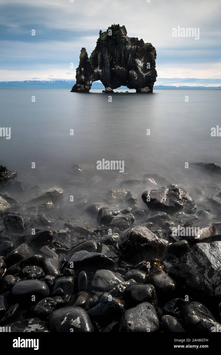 Symmetrical wide angle view of the Thirsty Dragon rock formation during a low tide and dark pebbles in the foreground Stock Photo