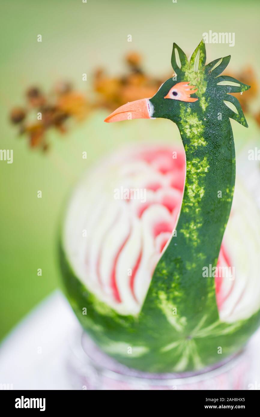 Close up of a watermelon carved like a peacock against a green bokeh background Stock Photo