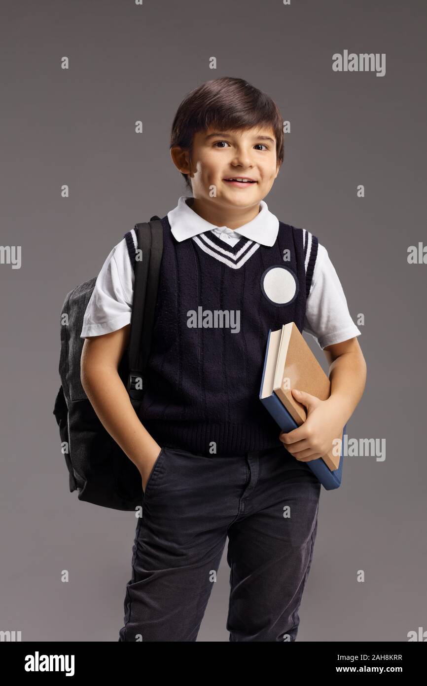 Boy in a school uniform holding books and smiling over a grey ...