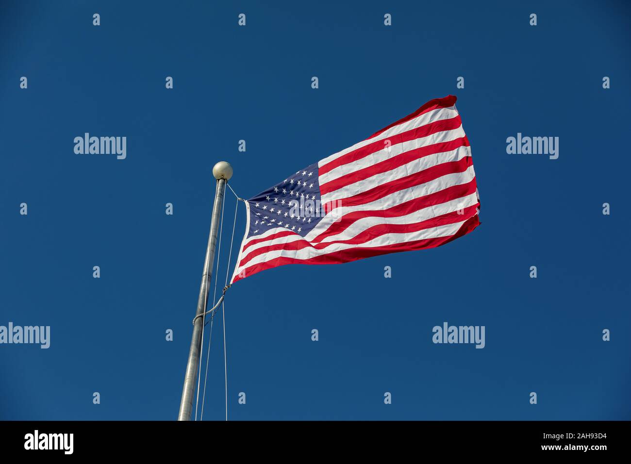 Looking up at large, new United States of America flag flying in the wind on a sunny day with deep blue sky in background Stock Photo