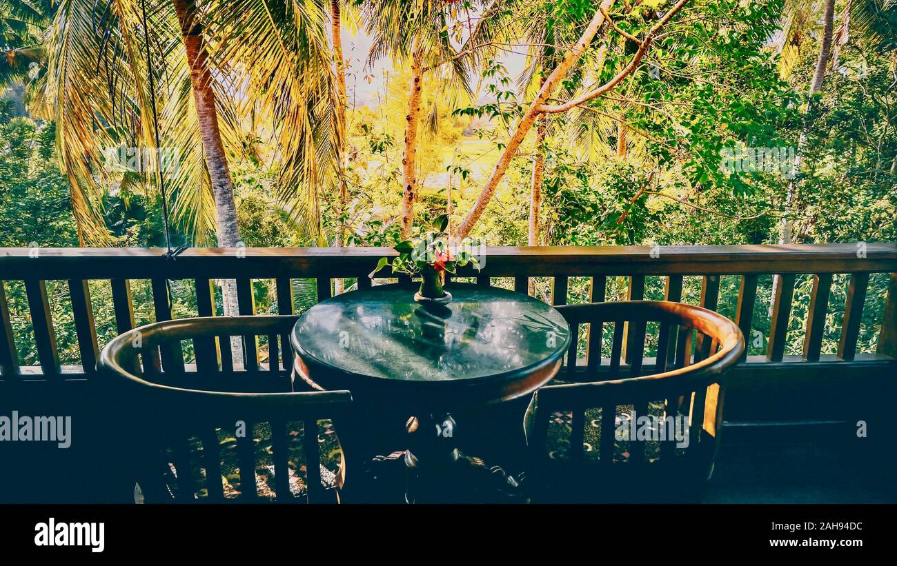 A table for two and a balcony railing in shadow, silhouetted against the bright tropical jungle in the background. Ubud, Bali. Stock Photo