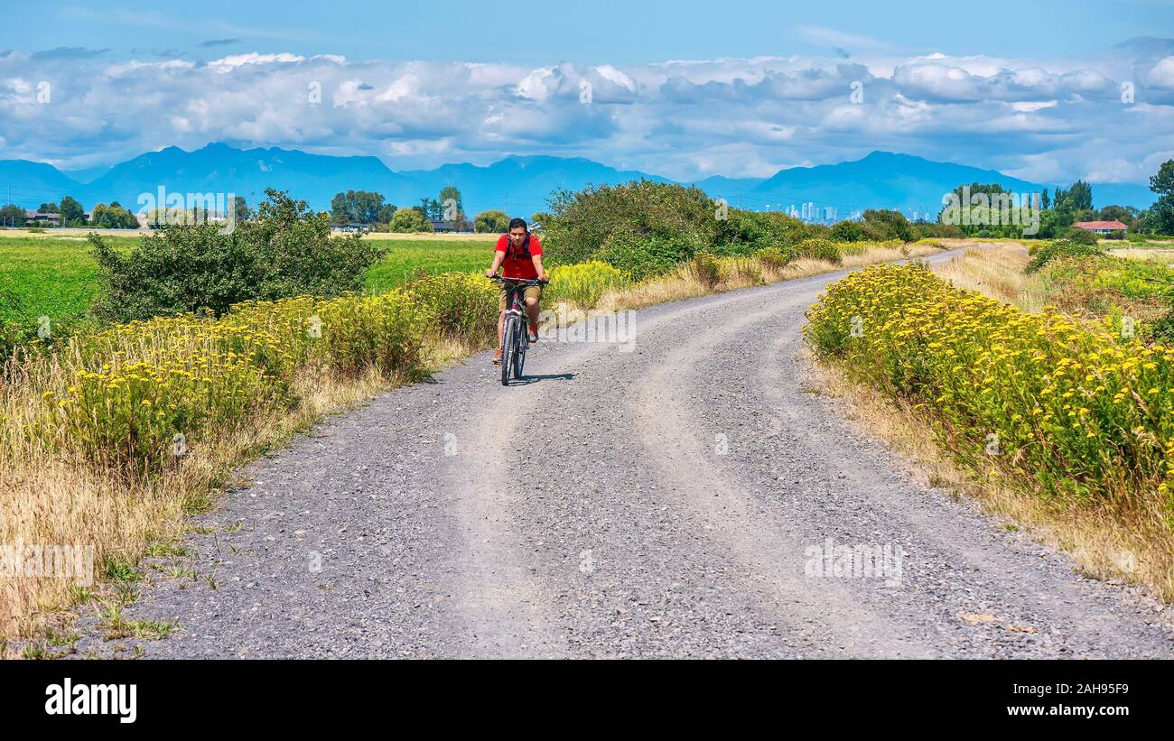 Delta, B.C., Canada - July 20, 2019. A young man rides a mountain bike without a helmet, on a gravel road in a rural setting near Vancouver. Stock Photo