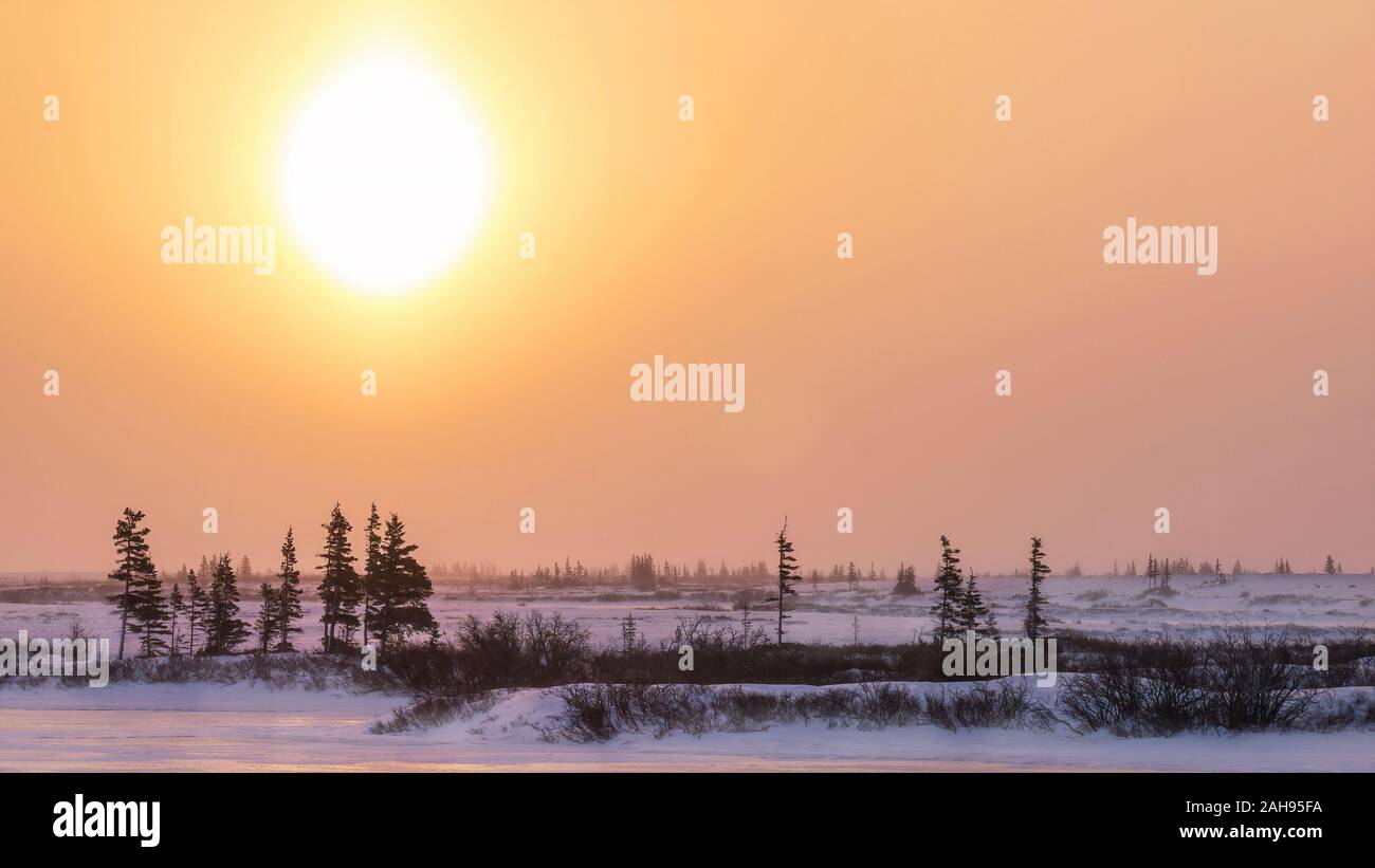 A cold winter landscape in northern Canada, as the atmospheric phenomenon known as a sun dog turns the sky orange near Churchill, Manitoba. Stock Photo