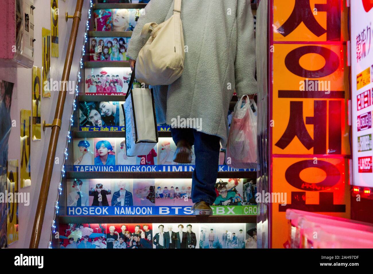 A woman carrying shopping bags climbs stairs with pictures of Korean idols and celebrities on them in a shop in Shin-Okubo, Shinjuku, Tokyo, Japan. Stock Photo