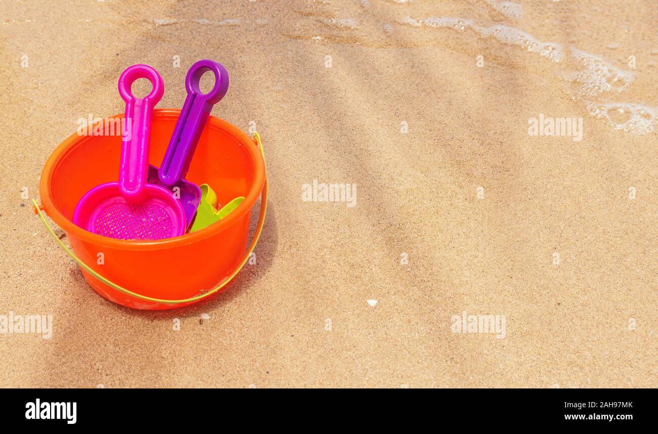 A summer vacation scene with a brightly colored child's plastic pail and shovels on a fine sandy beach, and faint shadow of a palm frond. Copy space. Stock Photo
