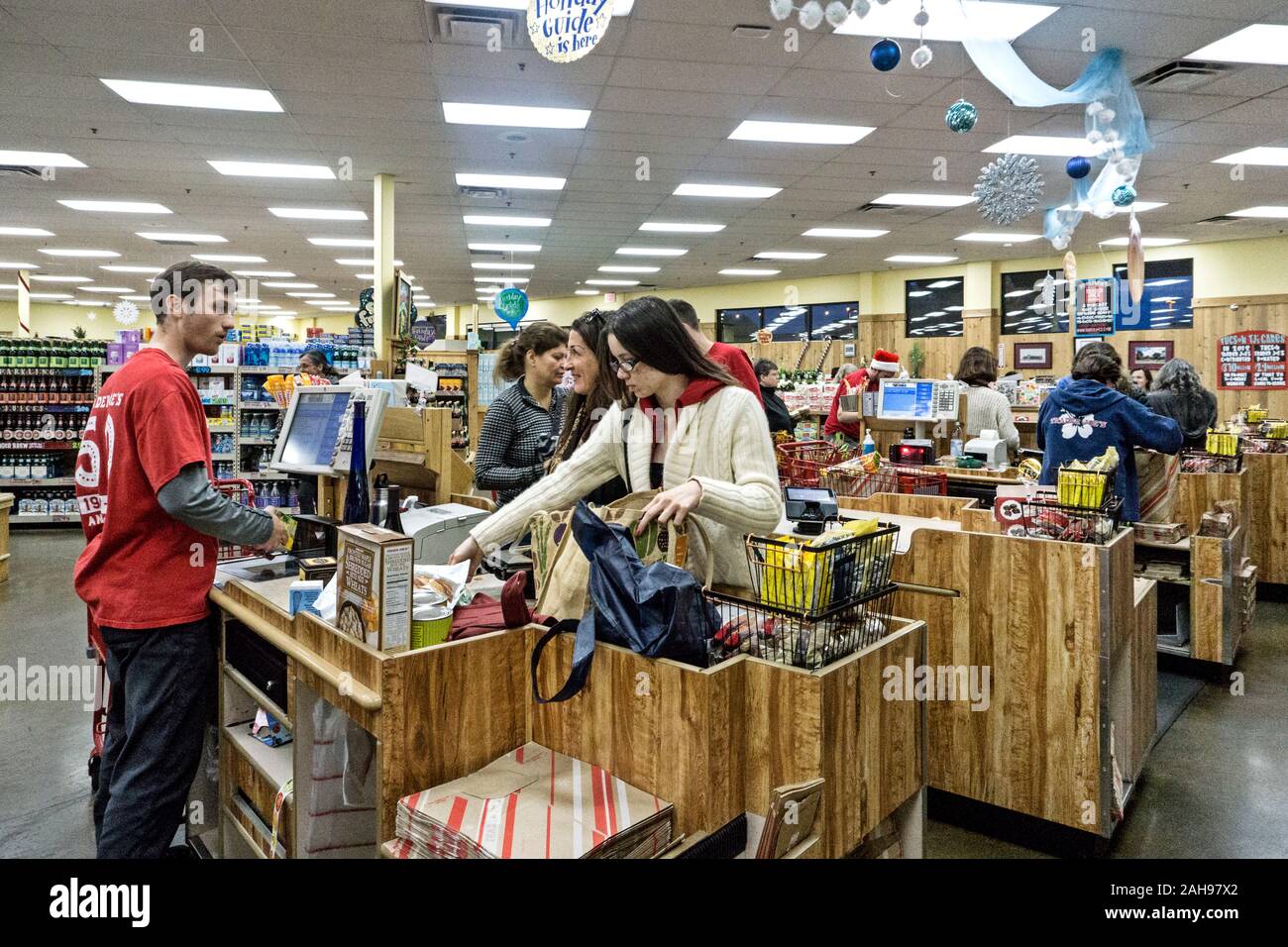 view toward exit side row of faux wood check-out stands at Trader Joes  decorated for Christmas with pretty hanging baubles & crowded with shoppers Stock Photo